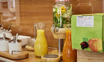 A selection of drinks on a wooden surface. There are fresh juices in glass carafes and a box with apple juice.