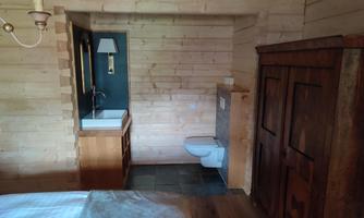 A cozy room with wooden walls and a bathroom area. There is a sink, a toilet, and a wooden wardrobe.