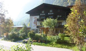 A picturesque inn with a large garden and mountain views. The facade features a mural and is surrounded by trees.