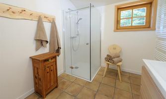 Bathroom with a glass shower and natural wood. Towels, a stool, and a small wooden cabinet are in the room.