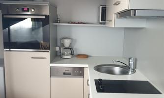 A modern kitchenette with light-colored cabinets and a stove. The amenities include a refrigerator, a coffee machine, and a sink.