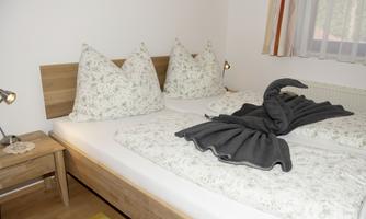 A cozy bedroom with a double bed and decorative pillows. On the bed lies an intricately folded towel in the shape of a swan.