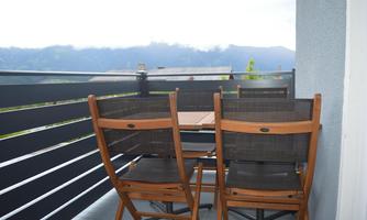A balcony with a small table and two wooden chairs. In the background, there are mountains and a cloudy sky.