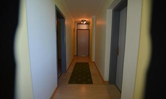 A long corridor with bright walls and a carpet. At the end of the corridor, there is a closed door.
