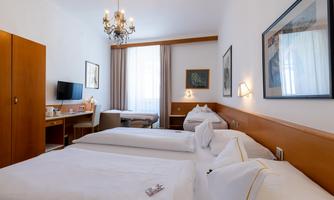 A bright hotel room with two single beds and a cozy atmosphere. There is a television, a table, and a beautiful chandelier.