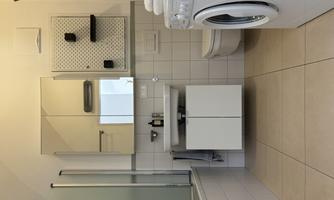 A modern bathroom with a bathtub, a sink, and a washing machine. The walls are brightly tiled, and there is a mirror above the sink.