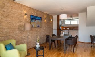 A modern dining room with wooden flooring and a stylish stone wall. A table with chairs and a cozy seating area are well arranged.