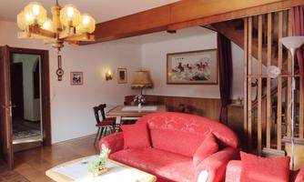 A cozy living room with a red sofa and a wooden table. In the background, there is a staircase and an inviting dining area.