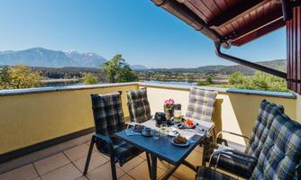 A cozy balcony with a table and chairs. In the background, the mountains and a green landscape can be seen.