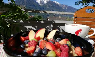 A delicious fruit salad with apples, berries, and grapes in front of an impressive mountain backdrop. In the background, a cup of coffee is visible.