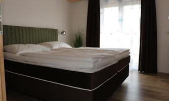 A cozy bedroom with a large double bed and bright curtains. The wooden floors give the room a warm atmosphere.