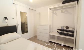 A modern bedroom with a double bed, a wardrobe, and a desk. The walls are bright, and the room feels friendly and inviting.