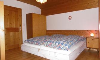 A cozy bedroom with a large bed and a colorful blanket. The room features wooden paneling and simple furniture.