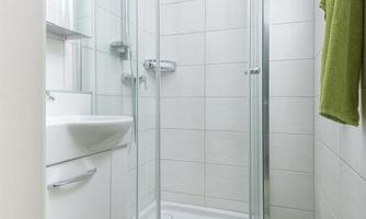 A modern bathroom with a shower cubicle and bright tiles. A green shower mat and towels add color to the room.