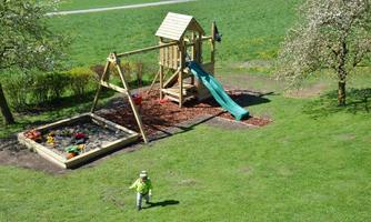 A beautiful playground with a slide, swing, and a sandbox. In the background, there is a lot of green grass and trees.