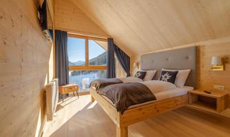 A cozy bedroom with wooden walls and two beds. Large windows offer a view of the mountains and bring in plenty of daylight.