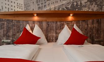 A cozy bed with red cushions and a wooden paneling. The soft lighting creates an inviting atmosphere.