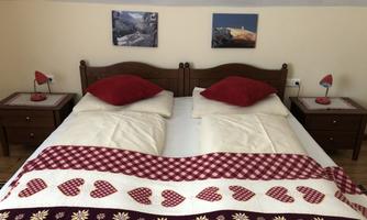 A cozy bedroom with two beds and red pillows. Pictures hang on the walls and small nightstands with lamps.