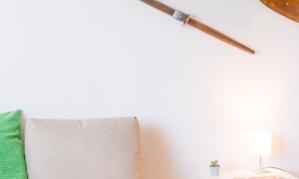 A cozy living room with a beige sofa and a small table lamp. Two wooden oars hang on the wall, giving the room a maritime flair.