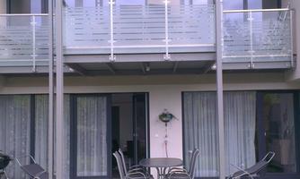 A modern residential building with two balconies. The garden is well-maintained and offers space for seating.