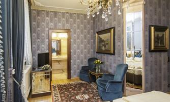 An elegant room with blue furniture, a large mirror, and a beautiful ceiling. The walls are decoratively styled with a classic pattern.