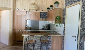 A modern kitchen with wooden ceilings and light furniture. Two chairs are at a small table, surrounded by a cozy atmosphere.