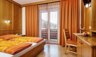 A cozy bedroom with orange curtains and bedding. A table with a chair and a fruit basket complements the decor.