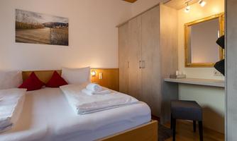 A cozy bedroom with a double bed and red pillows. There is a mirror on the wall and a desk stands next to it.