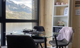 A modern room with a glass table and black chairs. Through the large window, you can see mountains and a beautiful landscape.