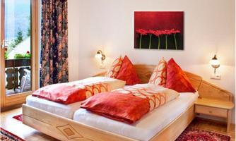 A cozy bedroom with two beds and red pillows. The room has large windows and decorative curtains.