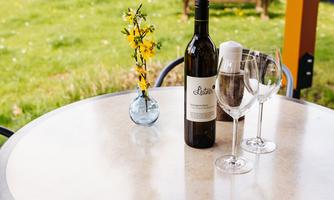 A bottle of wine is on a table next to two glasses. There is also a small vase with yellow flowers on the table.
