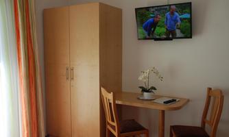 A simple room with a wooden wardrobe, a table, and two chairs. There is a television on the wall.