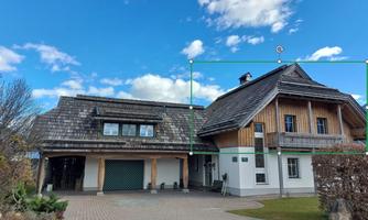 A modern house with wooden cladding and a sloping roof. The sky is clear and there is a green environment.