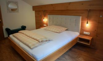A modern bedroom with a large bed and wooden paneling.  
Soft light sources create a cozy atmosphere.