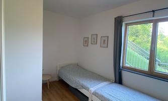 A simple bedroom with a single bed and a window. The walls are light, and there are some pictures on the wall.