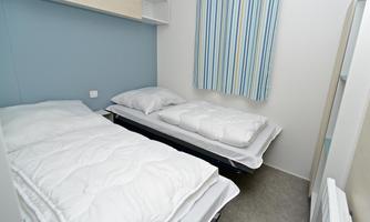 A simple room with two single beds. The walls are light blue and a striped curtain hangs at the window.