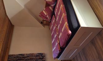 A cozy bedroom with a double bed and colorful pillows. The room has a wooden floor and a window with curtains.