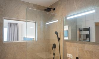 A modern bathroom with a large walk-in shower and an elegant sink. The room has bright tiles and is well-lit.