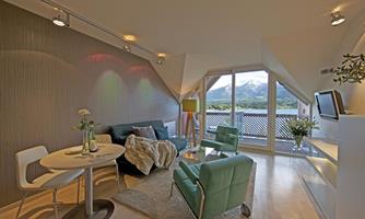 A modern living room with large windows and a view of the mountains. There are comfortable furniture and a cozy atmosphere.