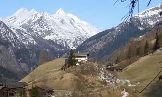 A picturesque mountain landscape with snow-capped peaks and gentle hills. In the foreground stands a large house in a tranquil setting.