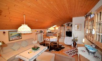 A cozy living room with a wooden ceiling and classic furnishings. The room is bright and inviting, with a dining table and a comfortable couch.