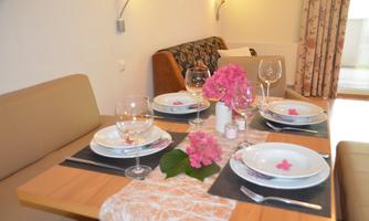 A stylishly set dining area with flowers and glasses. The table is adorned with white plates and a decorative table runner.
