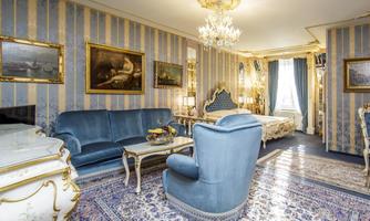 An elegant room with blue walls and golden accents. The furnishings include comfortable furniture, a beautiful carpet, and artworks on the walls.
