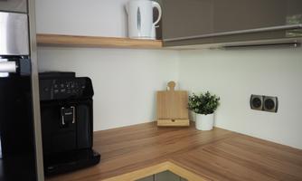 A modern kitchen with a coffee machine on a wooden countertop. In the background, there is a white jug and a green plant in a pot.