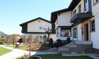 A modern house with a well-maintained garden and a clear blue sky in the background. The path leads to two stylish buildings.