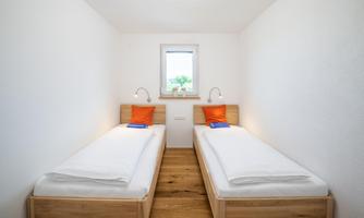 A cozy room with two single beds and orange cushions. The room has a large window with a view of the outside.
