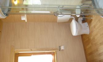 A bathroom with wooden walls and a modern shower area. There is a toilet and a sink, as well as a window for extra light.