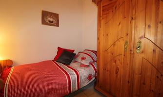 A small bedroom with a single bed and a wood-paneled wardrobe. The bedding is red with a checked pattern.