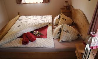 A cozy bedroom with a wooden bed and decorative pillows. On the bed lies a blanket and a beautiful bouquet of flowers.