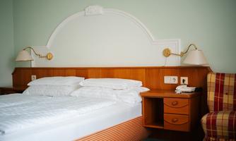 A cozy bedroom with a double bed and wooden furniture. Next to the bed is a chair with checked upholstery.